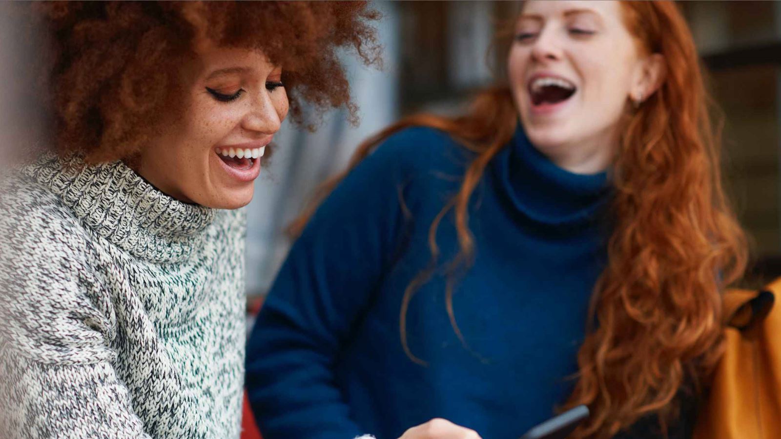 Two women laughing while one of them looks at her phone