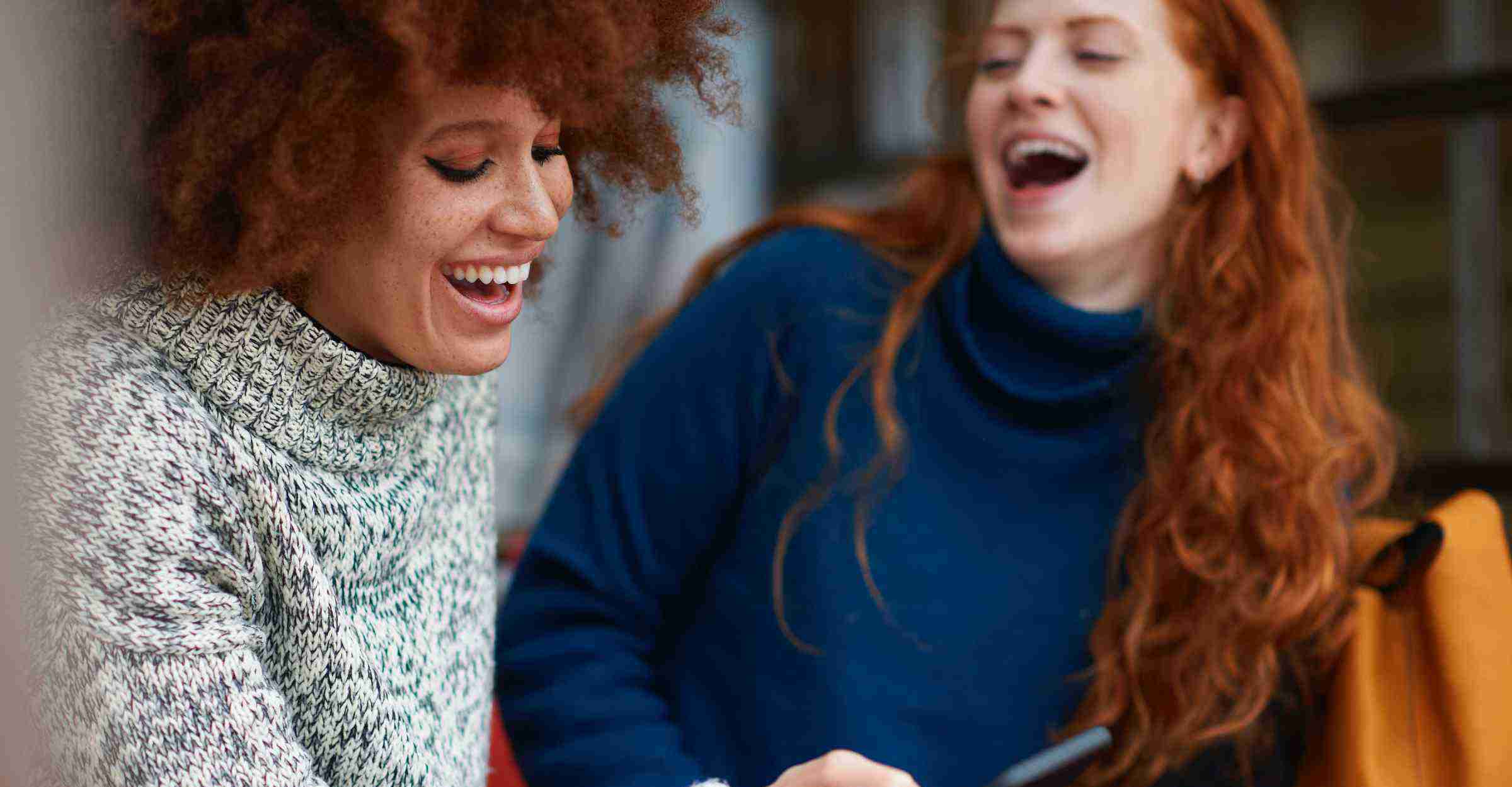 Two women laughing while one of them looks at her phone