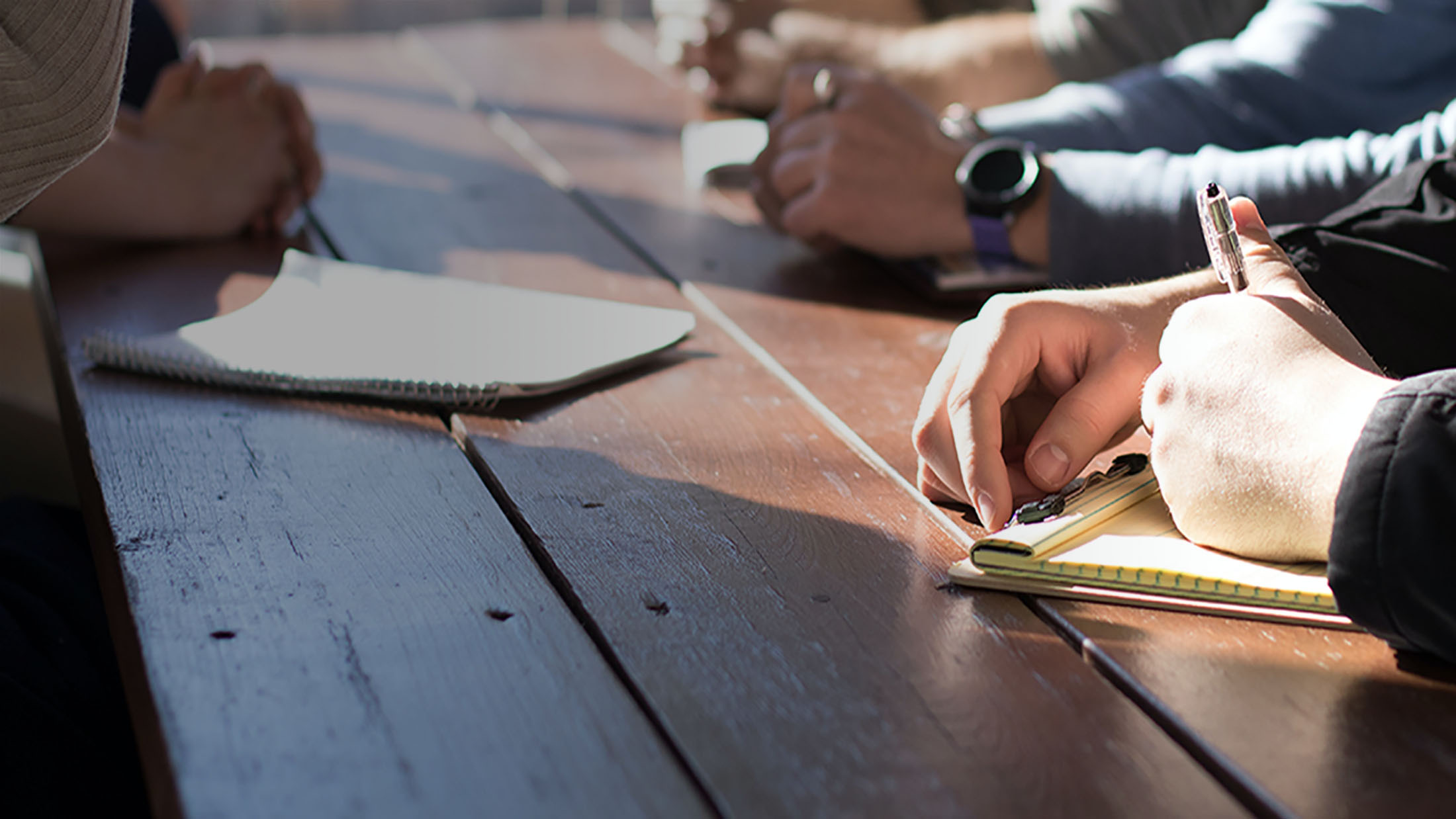 Close up of a desk with four people writing on notepads