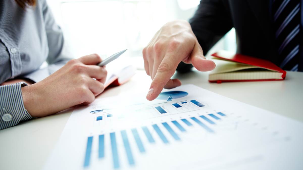 A desk with charts on and two peoples hands using pens on the charts