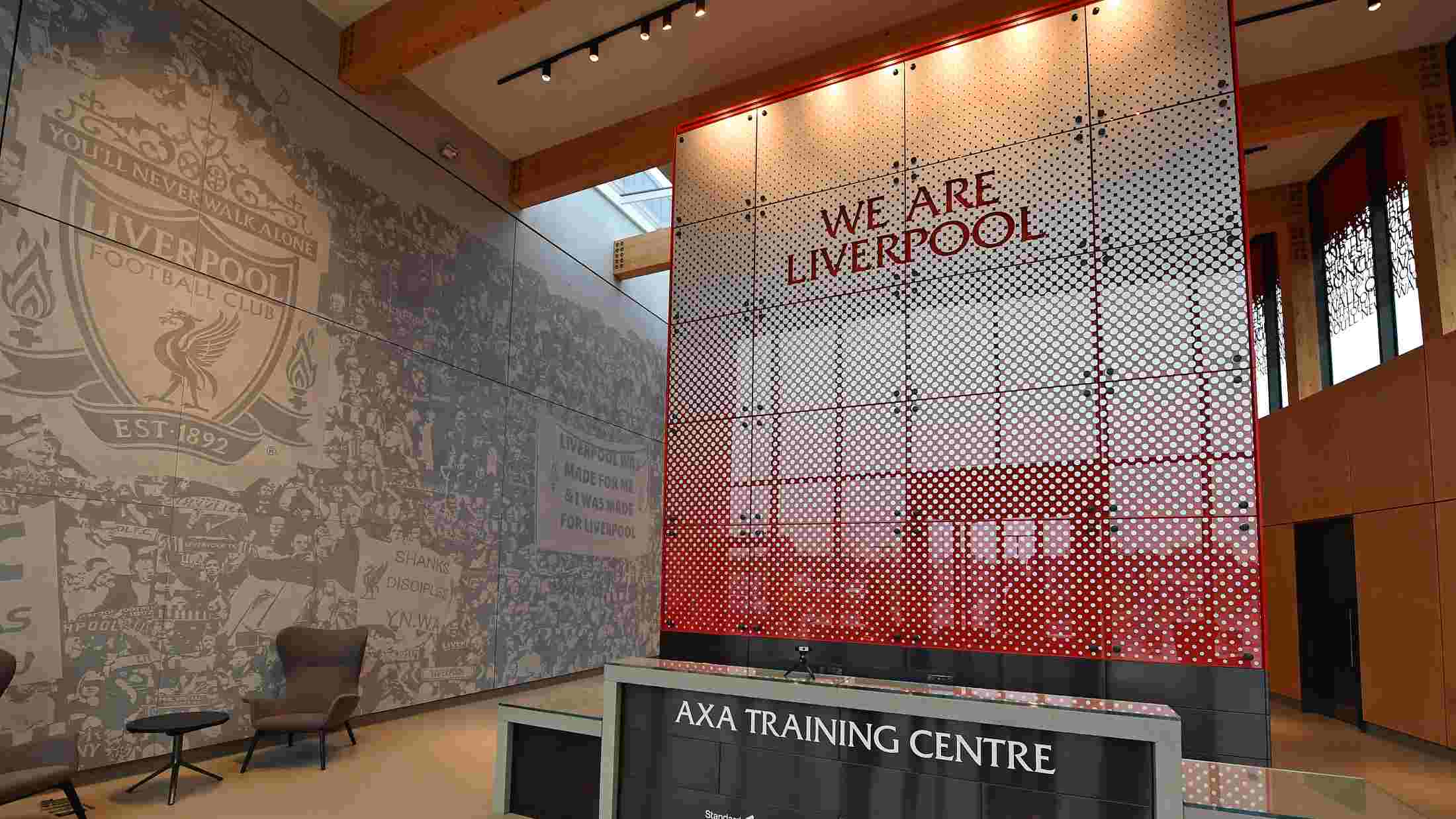 Inside the AXA Melwood Training Center, front desk with large wall backdrop red ombre saying 'We are Liverpool'