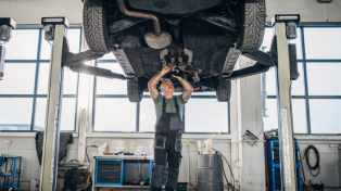 Mechanic underneath a car raised high above him fixing it