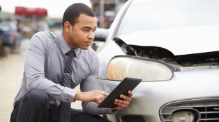 Man crouched next to a car with the bonnet up on his mobile phone