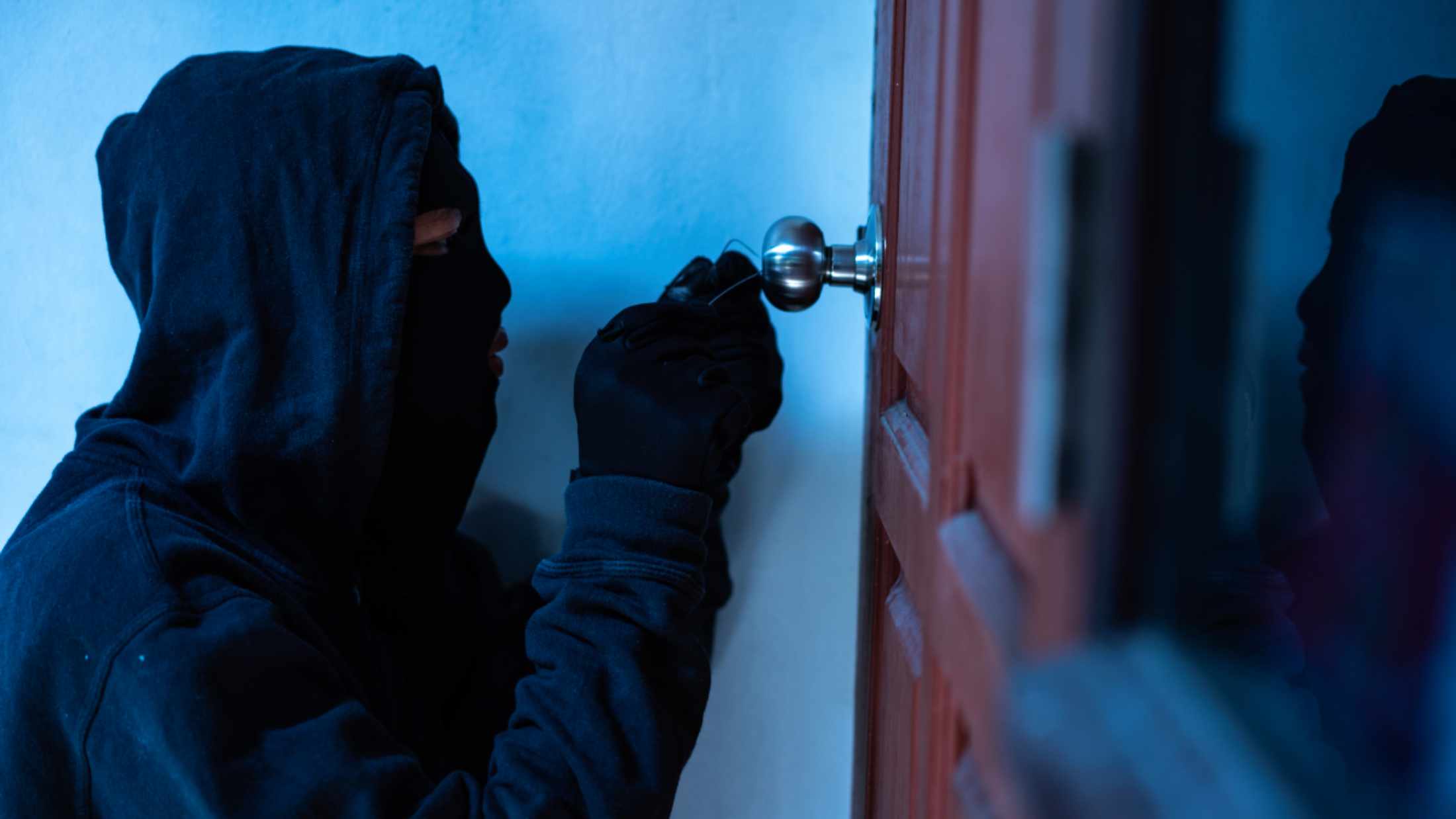 Masked thief using lock picker to open locked door