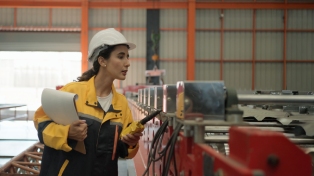 Factory inspector examining machinery wearing protective gear including a white hard hat