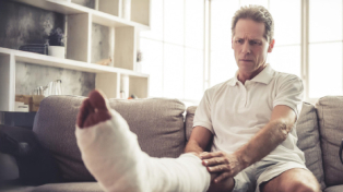 Man sat on his sofa with his broken and plastered leg up in front of him on a coffee table