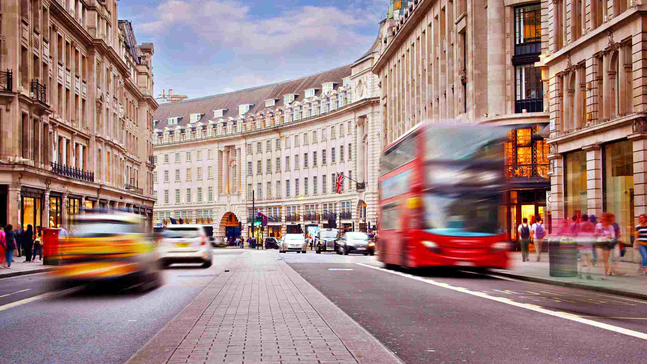 A busy Oxford Street in London with a red london bus, cars and taxis driving down and people walking down