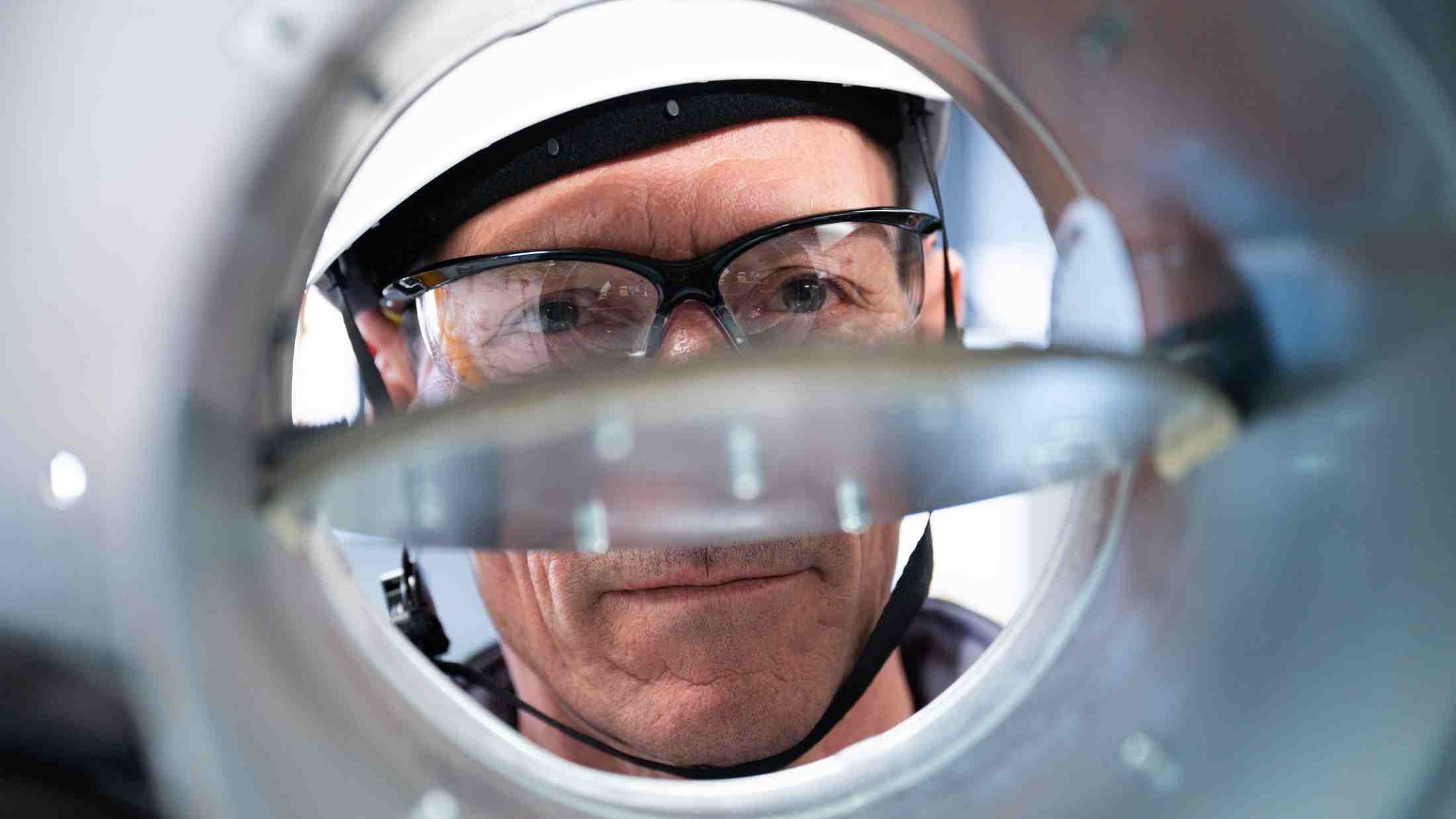 Scientist wearing a hard hat and protective glasses looking into a fire damper device