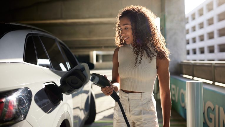 Young woman charging electric car at charging station