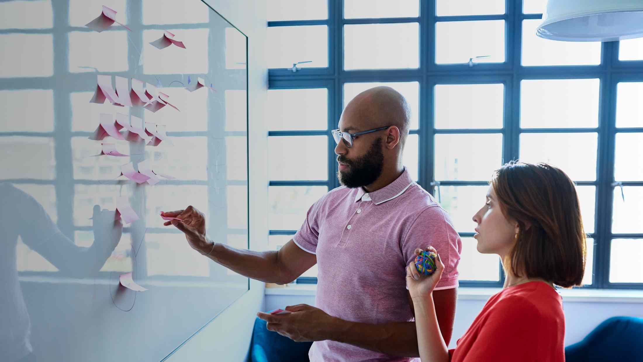 Two colleagues arrange post it notes on a whiteboard