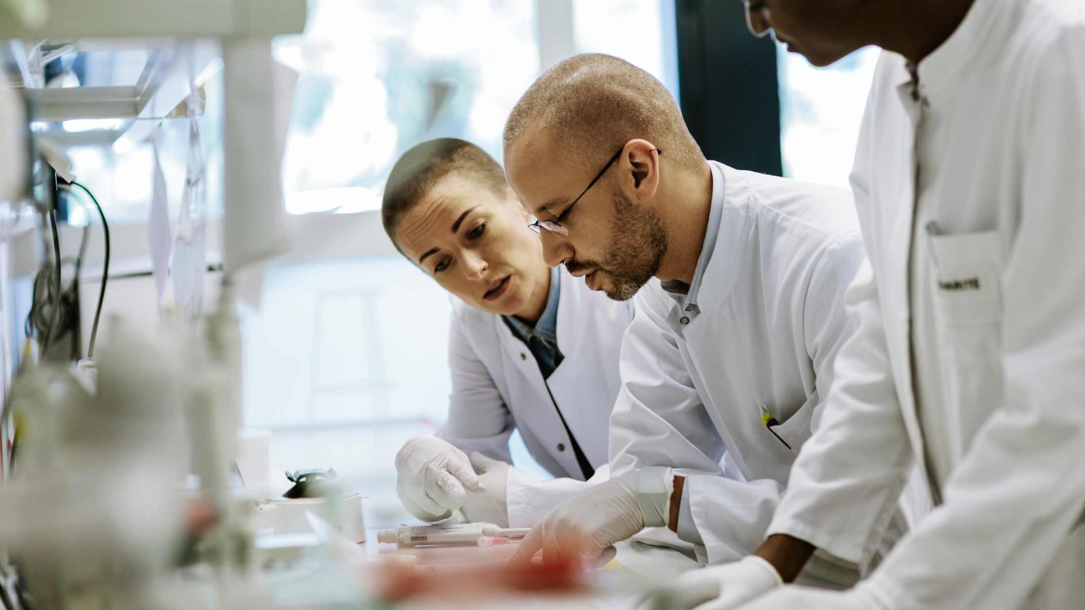 Three scientists working in a laboratory. They are bending over a table looking at data and a paper.