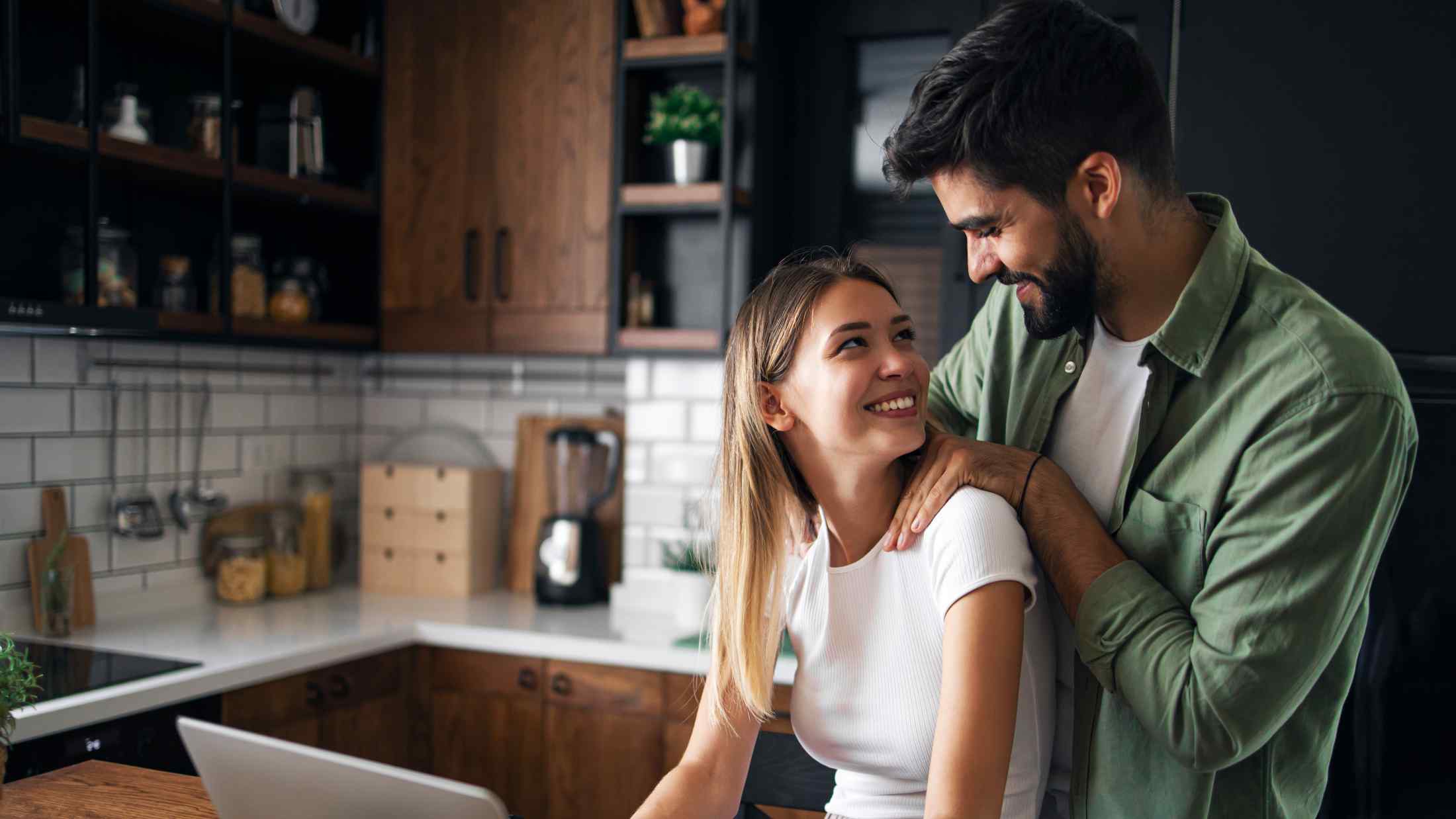Young couple sat at the kitchen table together on a laptop