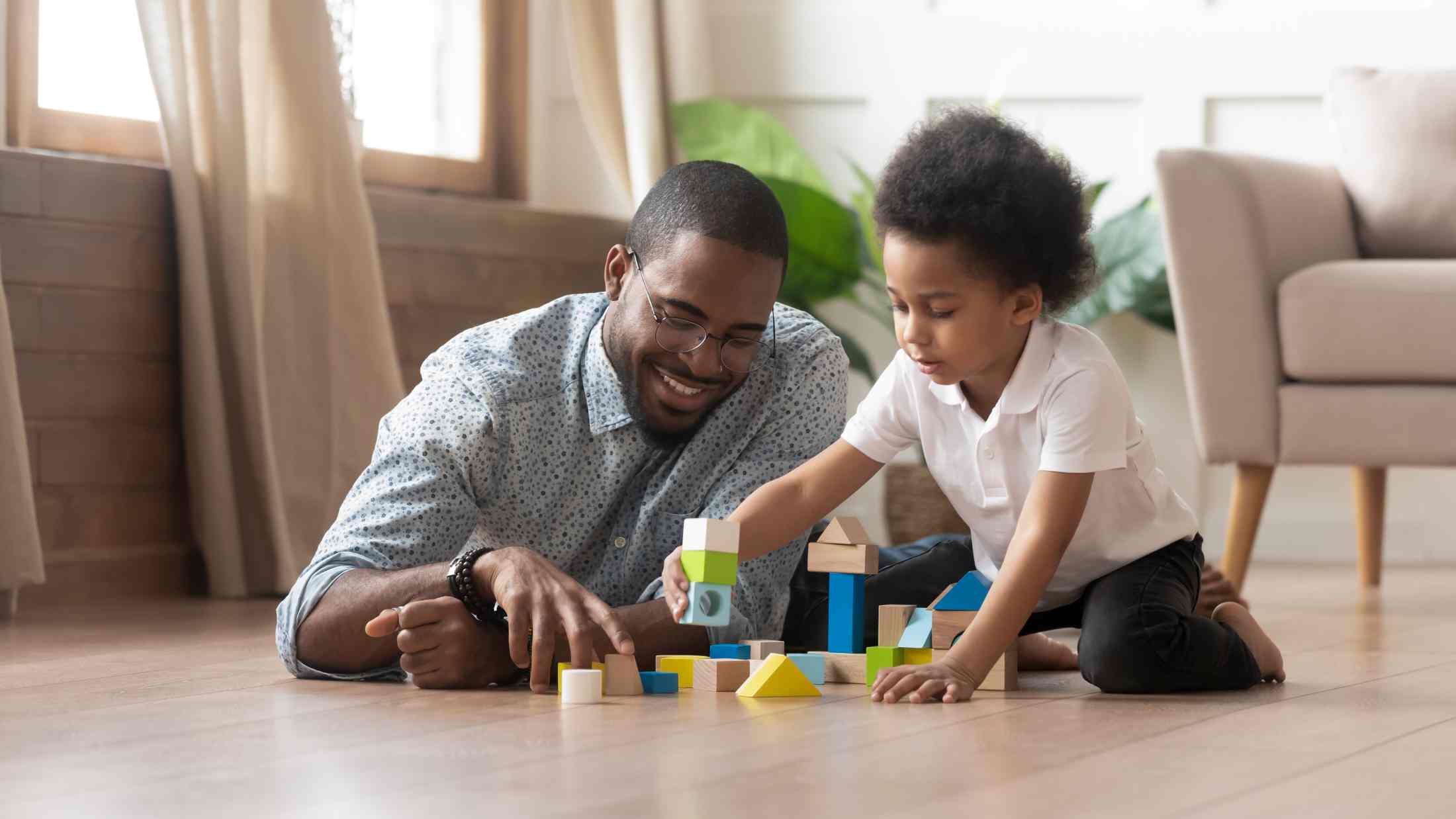 Father and young daughter playing with building blocks together on the living room floor
