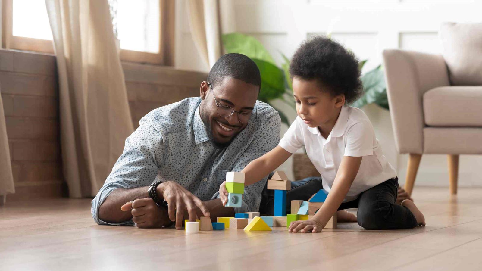 Father and young daughter playing with building blocks together on the living room floor