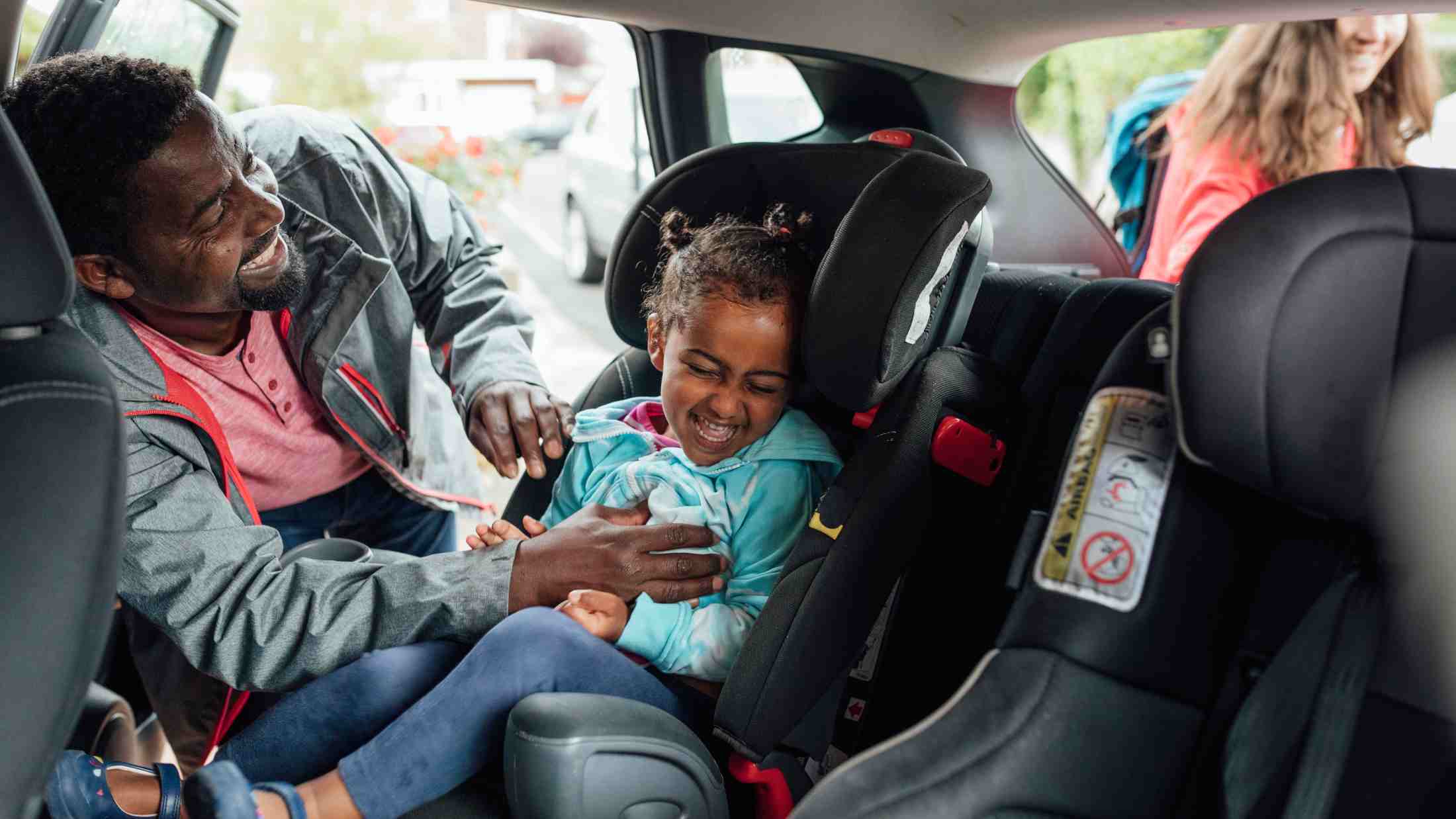 Dad buckling his young daughter into a car seat in the back of the car
