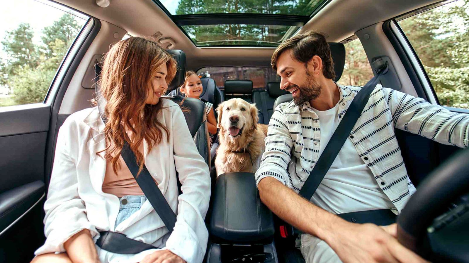 Mum, dad and young daughter sat in the car with their golden retriever dig sat between the front seats