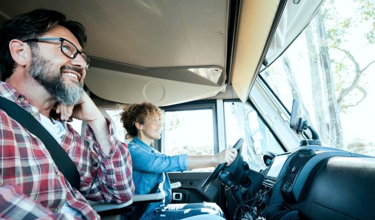 Couple driving a goods carrying vehicle such as a large van or lorry, smiling whilst looking out towards the road